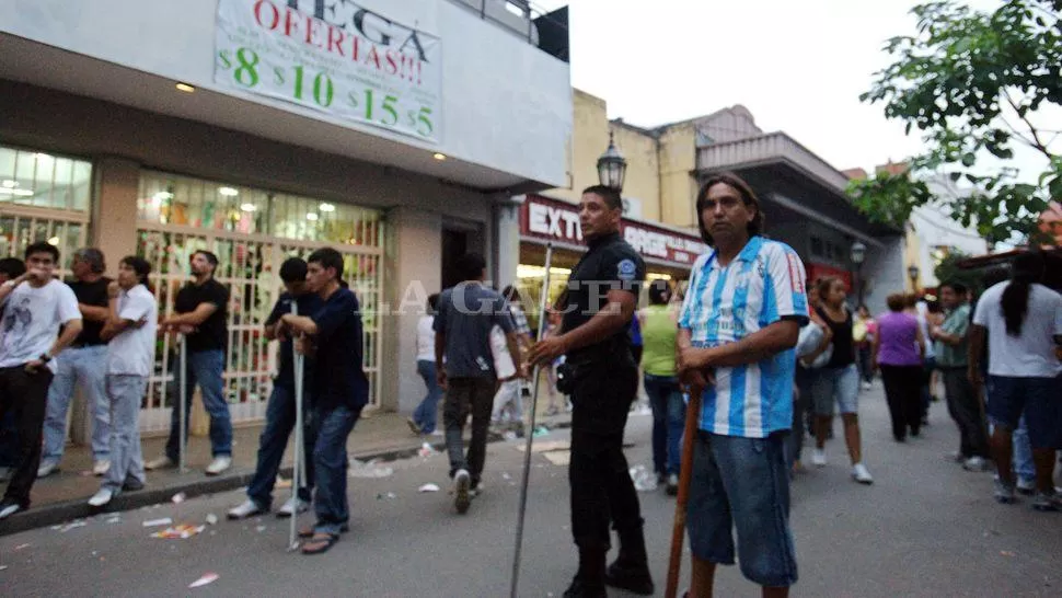 MOMENTOS TENSOS. Un policía sostiene un fierro junto a un vendedor ambulante. Más atrás, personal de un comercio se prepara. LA GACETA / FOTO DE OSCAR FERRONATO