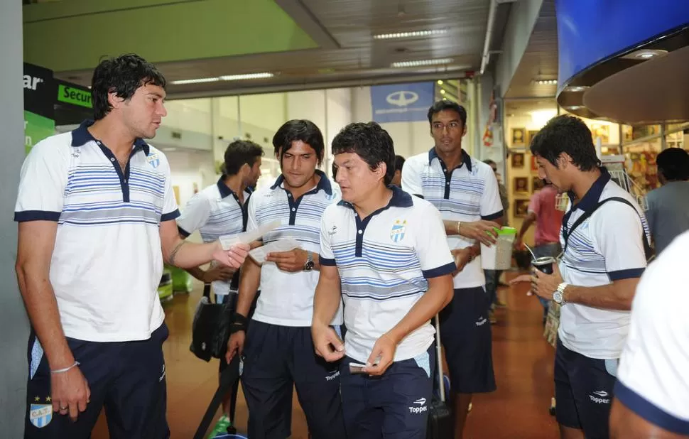 CHECK IN. Juan Pablo Pereyra le entrega los tickets del vuelo a Pulguita y Montiglio. More, alejado, matea con Herrera.