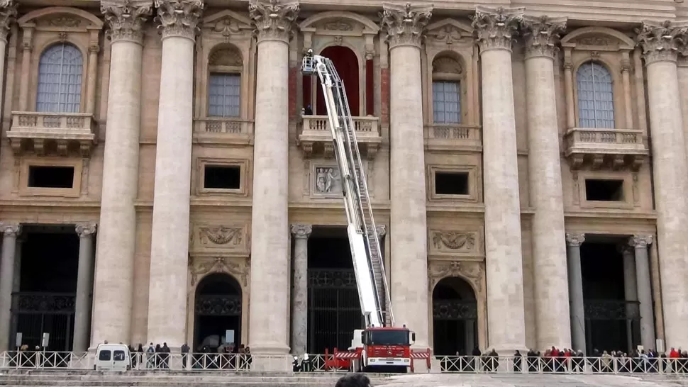 TERCIOPELO ROJO. Bomberos decoran el balcón central de la Basílica de San Pedro. EFE