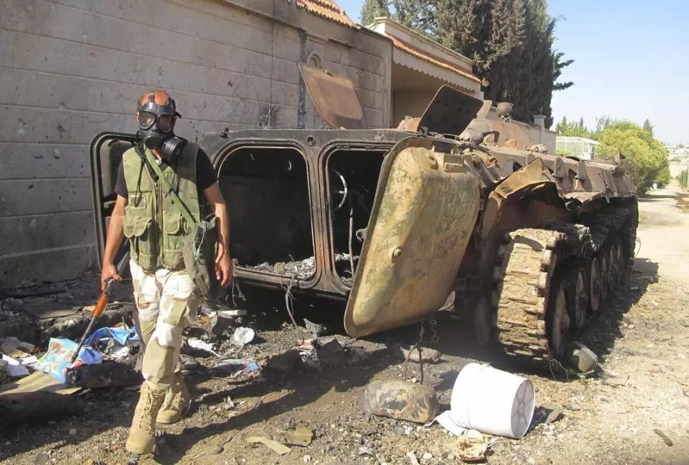 PROTEGIDO. Un soldado rebelde se cubre con una máscara antigases, mientras camina cerca de un destruido blindado del Ejército de Al Assad en Idlib. REUTERS