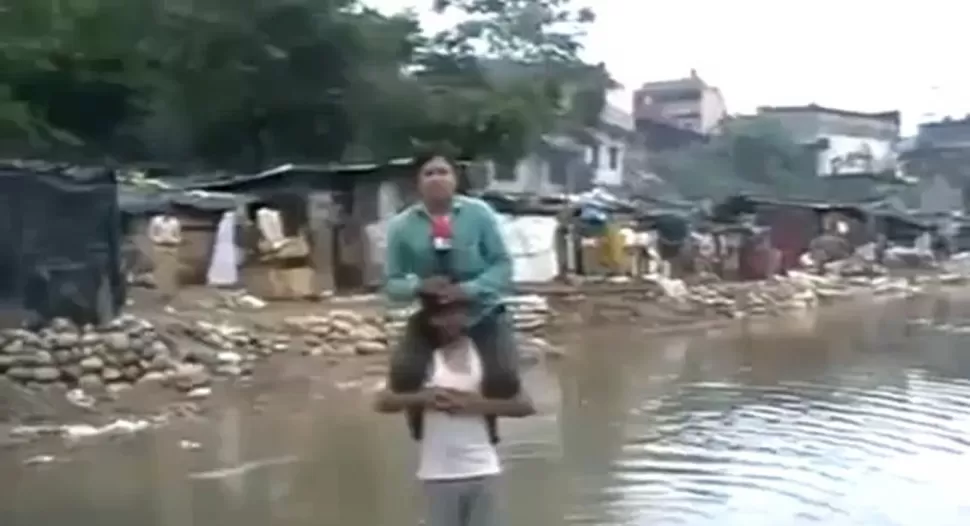 DESDE LOS HOMBROS. El reportero es sostenido por uno de los damnificados mientras reporta para su cadena de TV. CAPTURA DE VIDEO