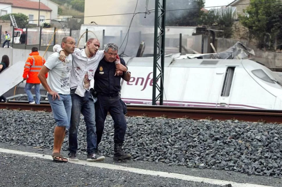 UN RESCATE. Uno de los heridos es ayudado por dos vecinos del lugar del accidente. El tren traccionaba ocho vagones y llevaba 218 pasajeros. FOTOS DE REUTERS