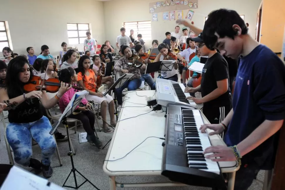 TODOS JUNTOS. En un aula grande, la orquesta se reúne a tocar la obra que han preparado durante la semana. 