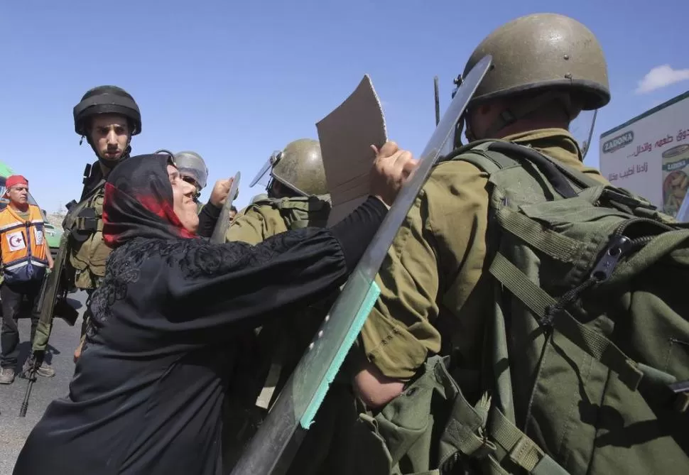 EN HAWARA. Una palestina golpea a un soldado israelí, en un puesto de control de Nablus, Cisjordania, en protesta por la ofensiva militar sobre Gaza. reuters