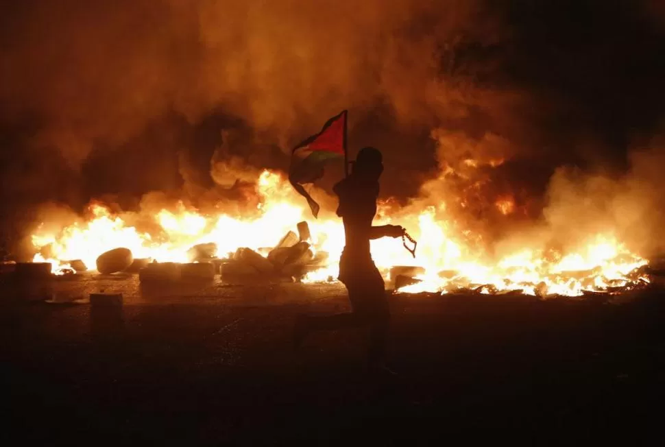 EN CALANDIA. Un joven agita una bandera palestina, en medio de las protestas realizada en la Cisjordania.    