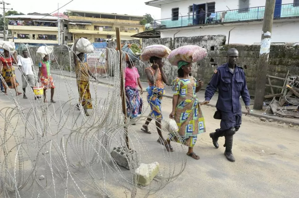 EN LIBERIA. Un policía escolta a mujeres, fuera de una zona en cuarentena. 