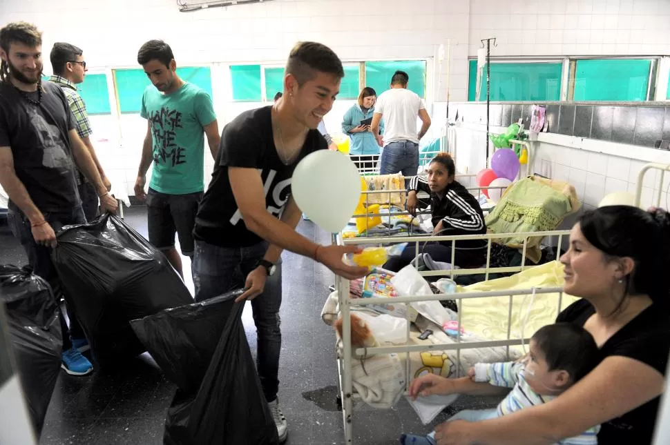 EMOCION. Leonardo Rizo le entrega un juguete a una madre que tiene a su hijo en brazos, mientras Esteban Goicoechea contempla la escena en el Hospital de Niños.  la gaceta / foto de hector peralta