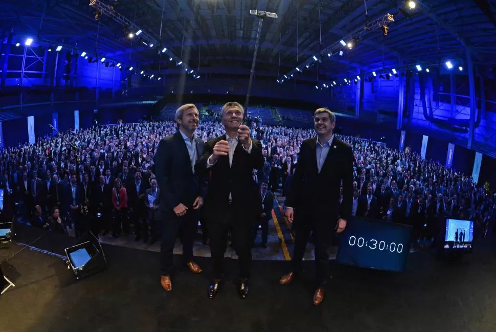 SELFIE PRESIDENCIAL. Mauricio Macri utiliza un palo para sacar una foto de la reunión de intendentes, flanqueado por el ministro de Interior, Rogelio Frigerio, y el jefe de Gabinete, Marcos Peña.  presidencia de la nación