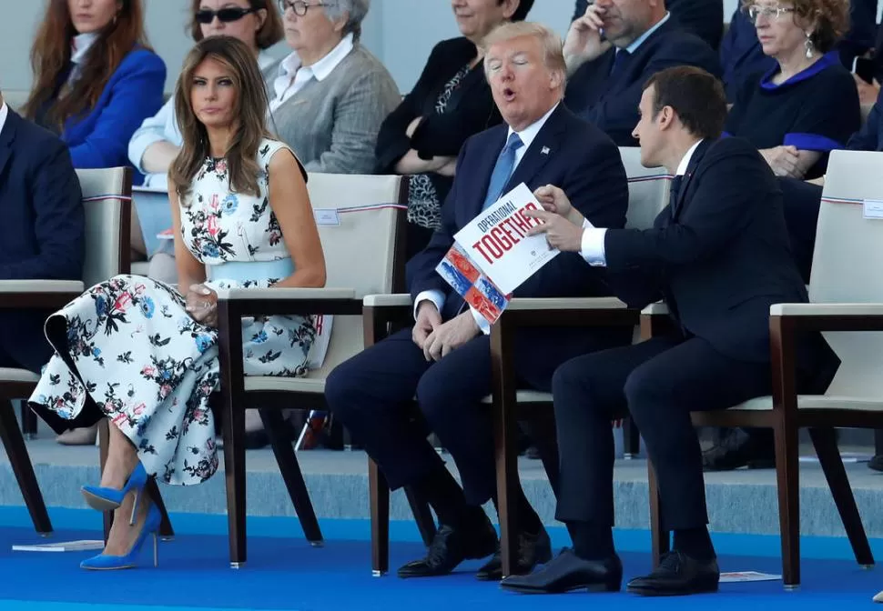 GESTOS. Emmanuel Macron y Donald Trump intercambian opiniones en presencia de Melania Trump durante el desfile militar del 14 de Julio. Reuters