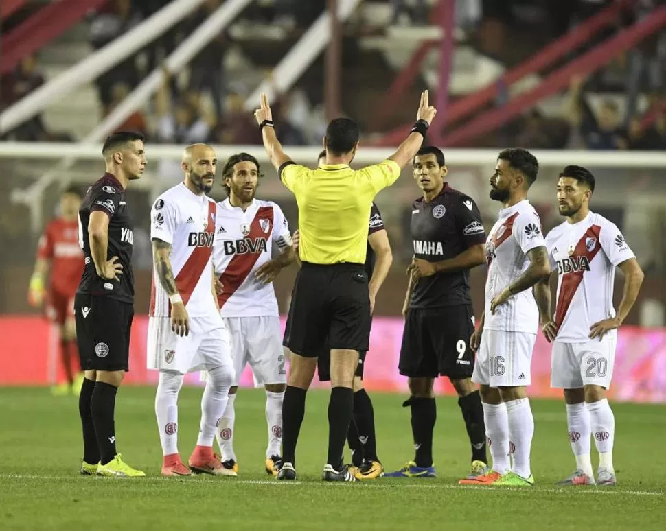 MOMENTO CLAVE DEL PARTIDO. El árbitro colombiano Wilmar Roldán solicita el VAR por la falta de Montiel a Pasquini y los jugadores de River y de Lanús lo rodean. Finalmente sancionó penal para el “Granate”. telam