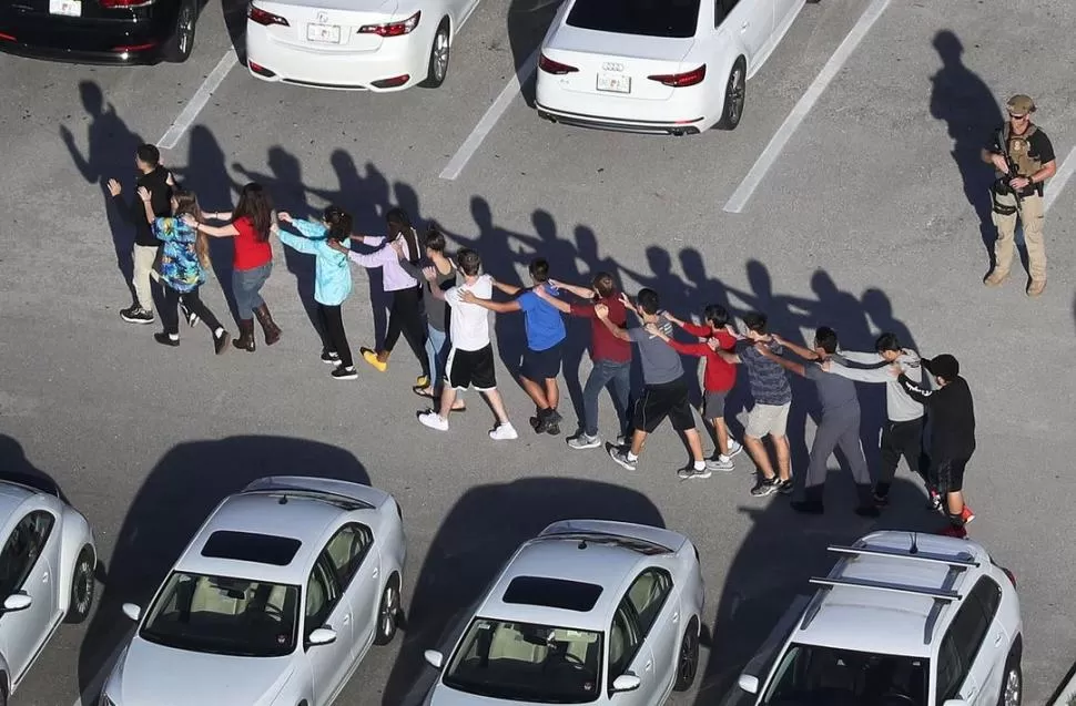 FILA INDIA. Estudiantes se retiran de la escuela ante la atenta mirada de la Policía, momentos después del tiroteo. telam 