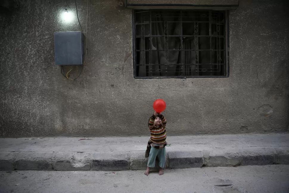FELIZ CON TAN POCO... Un niño descalzo juega feliz con un globo en la asediada ciudad siria de Duma. REUTERS