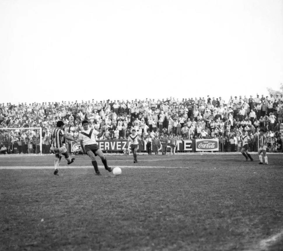 ESTADIO A PLENO. Juan “Malevo” Ferreyra (4) trata de despejar la pelota ante la marca de Eduardo Zóttola. Un partido histórico. 