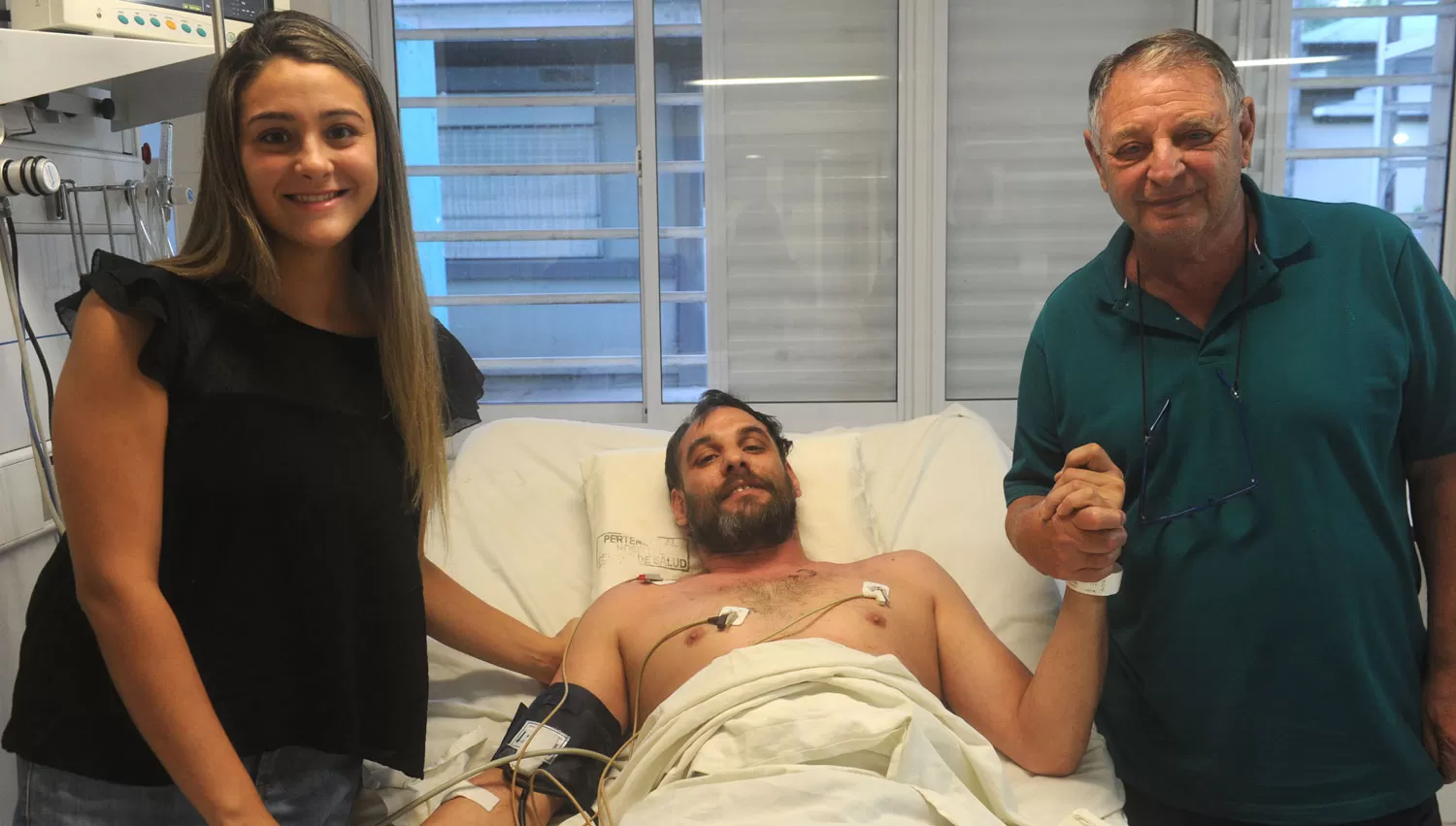 CON SU FAMILIA. La hermana y el padre de Maximiliano Conca lo sostienen de las manos durante la internación en el Centro de Salud.