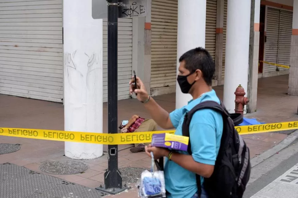 EN LA VEREDA. Un vendedor de barbijos saca fotos mientras pasa junto al cadáver de un hombre.  reuters