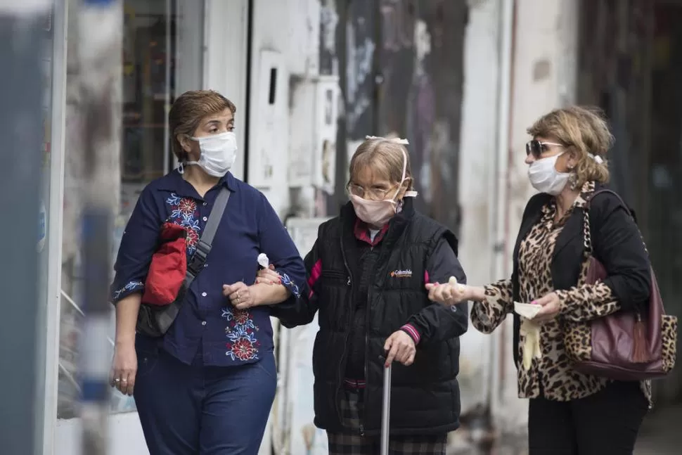 DEL BRAZO. Una mujer ayuda a caminar a otra que usa bastón y dialoga con una tercera.