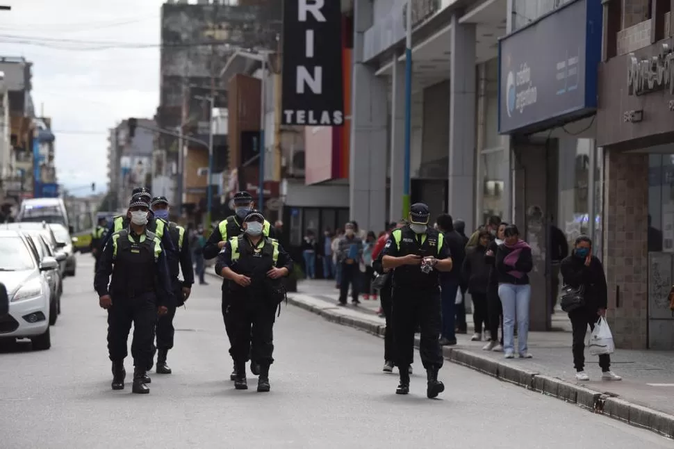 CONTROLES. Un grupo de policías patrulla el microcentro; de fondo, la gente hace cola para pagar cuentas.