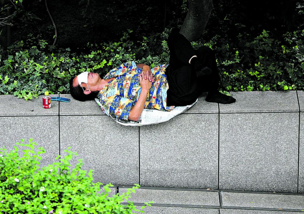 la siesta.- Con el barbijo como antifaz, un hombre se toma un descanso en una calle de Tokio.  fotos Reuters