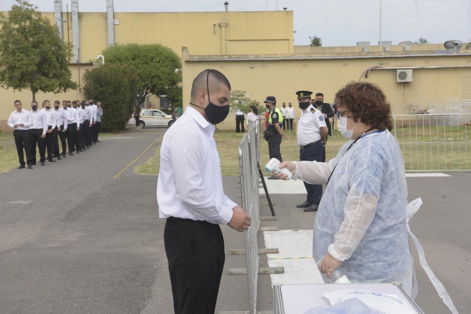 TEMPERATURA. Una agente sanitaria verifica que un cadete no tenga fiebre. Detrás, un policía observa la escena.