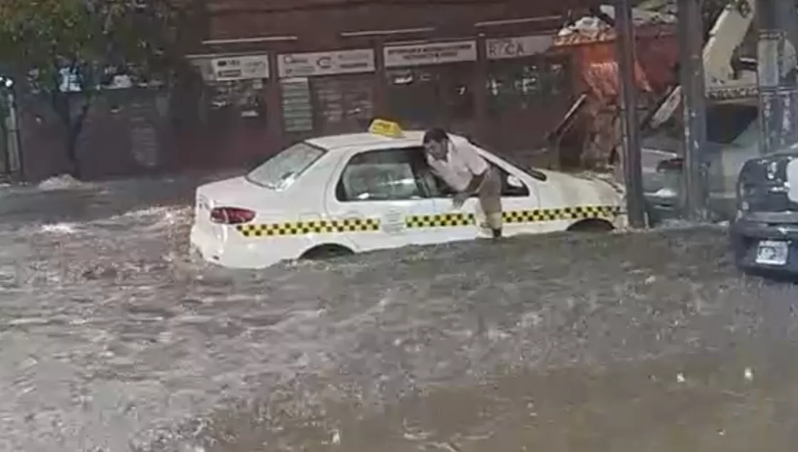 A RESGUARDO. Un taxista sale de su auto por la ventanilla del acompañante, debido a que el vehículo se estaba llenado de agua,