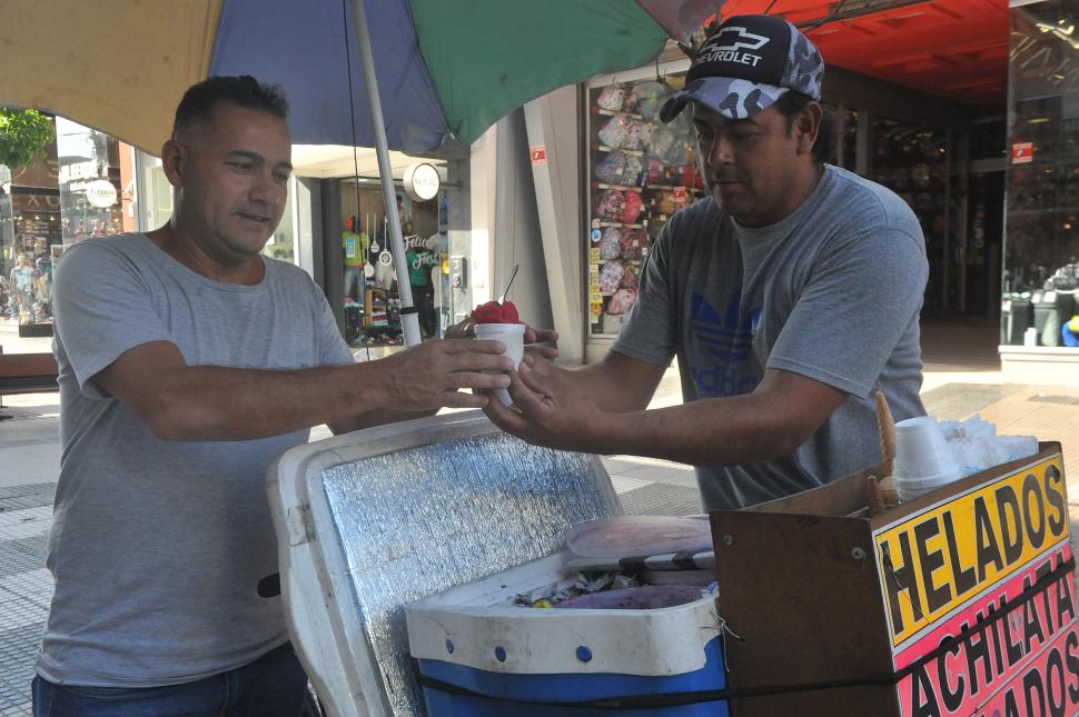 LA INFALTABLE ACHILATA. El dulce y rojo producto tradicional se vende en las calles, y tiene sus fanáticos. En la imagen, el vendedor y el comprador, que lo mira con fruición, no tienen barbijos.