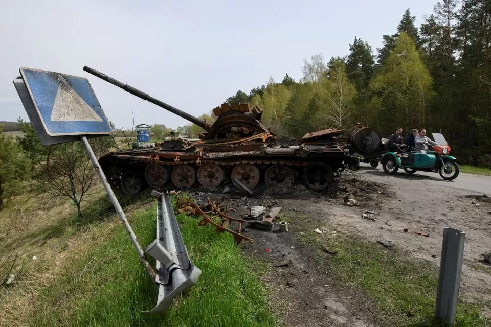 Civiles pasan en motocicleta por los escombros de la maquinaria militar rusa destruida durante la invasión rusa de Ucrania, en el pueblo de Rusaniv, región de Kiev. Foto de Reuters