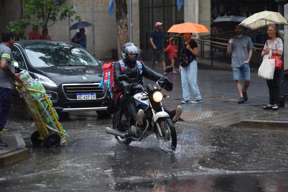 DE VEREDA A VEREDA. Un repartidor de comida intenta no mojarse más de lo inevitable en su recorrido.