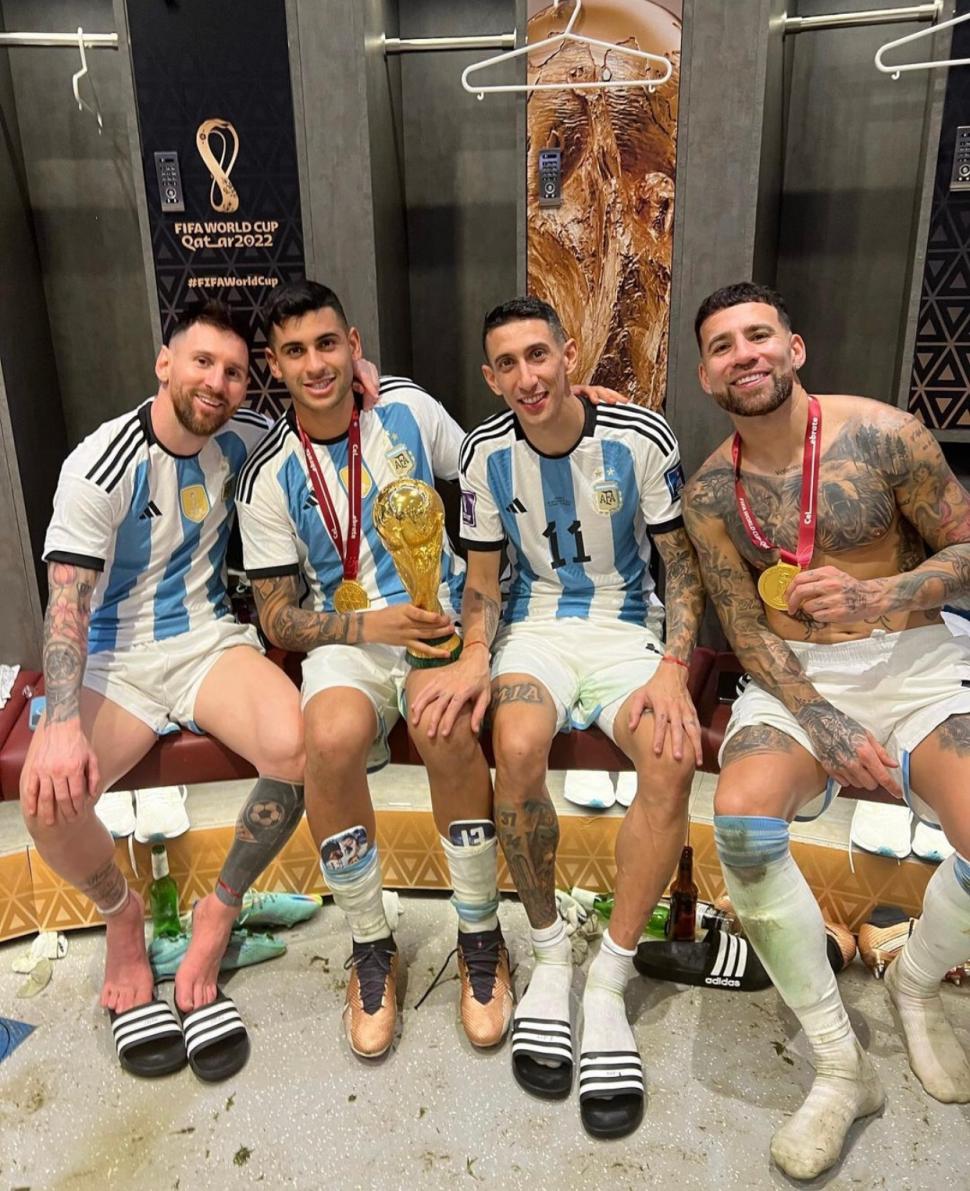 EN EL VESTUARIO. Lionel Messi, Cristian Romero, Ángel Di María y Nicolás Otamendi lucen el trofeo, que no conservarán, pero sí las medallas que serán el recuerdo que podrán tener en sus vitrinas.  