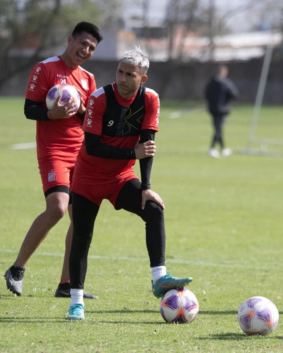 BUEN CLIMA DE TRABAJO. Brian Andrada pisa la pelota, muy serio, mientras detrás Gustavo Abregú suelta la carcajada. 