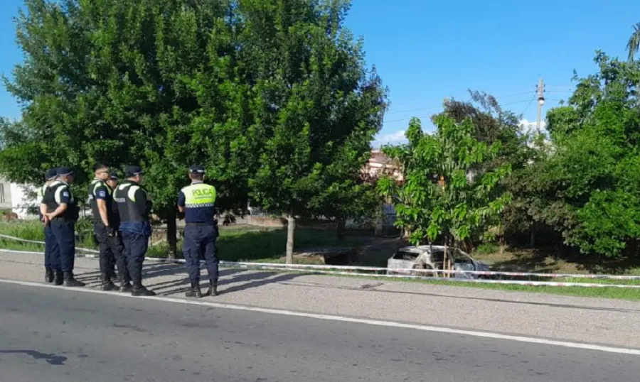 Policías custodian el lugar donde se encuentra el auto incendiado. 