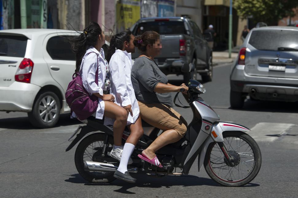 DE A TRES. Una madre traslada a dos alumnas en moto y sin casco.