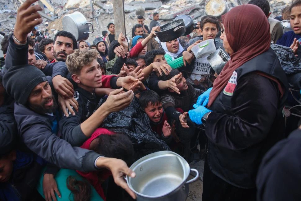 SUPERVIVENCIA. Adultos y niños pujan para alcanzar un plato de comida en una cocina comunitaria de Beit Lahia, en la devastada Franja de Gaza.  