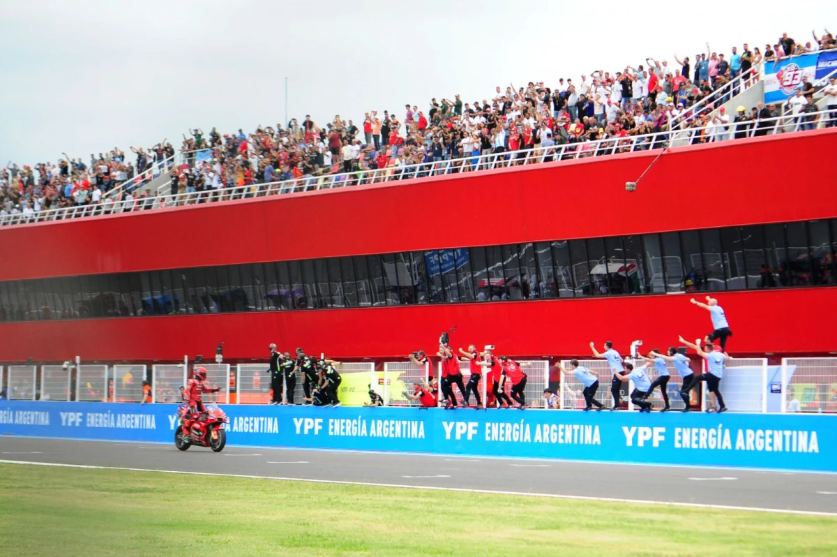 TRIUNFO. Márquez llega a la meta en la recta principal. Los mecánicos de su equipo lo alientan desde la reja y el público en el techo del paddock observa. FOTO DE DIEGO ARÁOZ