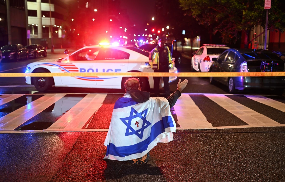 CONMOCIÓN. Un hombre envuelto en la bandera de Israel, que lleva una cruz y el nombre Jesús en el centro, gesticula mientras agentes de la Policía Metropolitana aseguran el área frente al Museo Judío. AFP