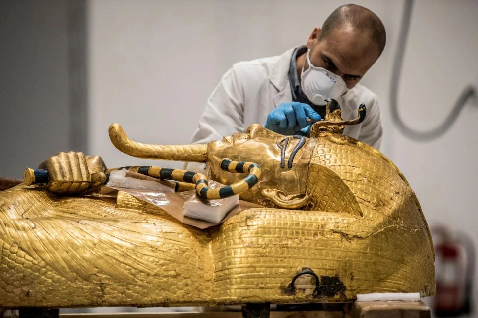 TAREA MINUCIOSA. Un arqueólogo egipcio trabaja en la restauración del sarcófago dorado del faraón Tutankamón, en un laboratorio de Guiza. La imagen había sido tomada el 13 de abril de 2020.