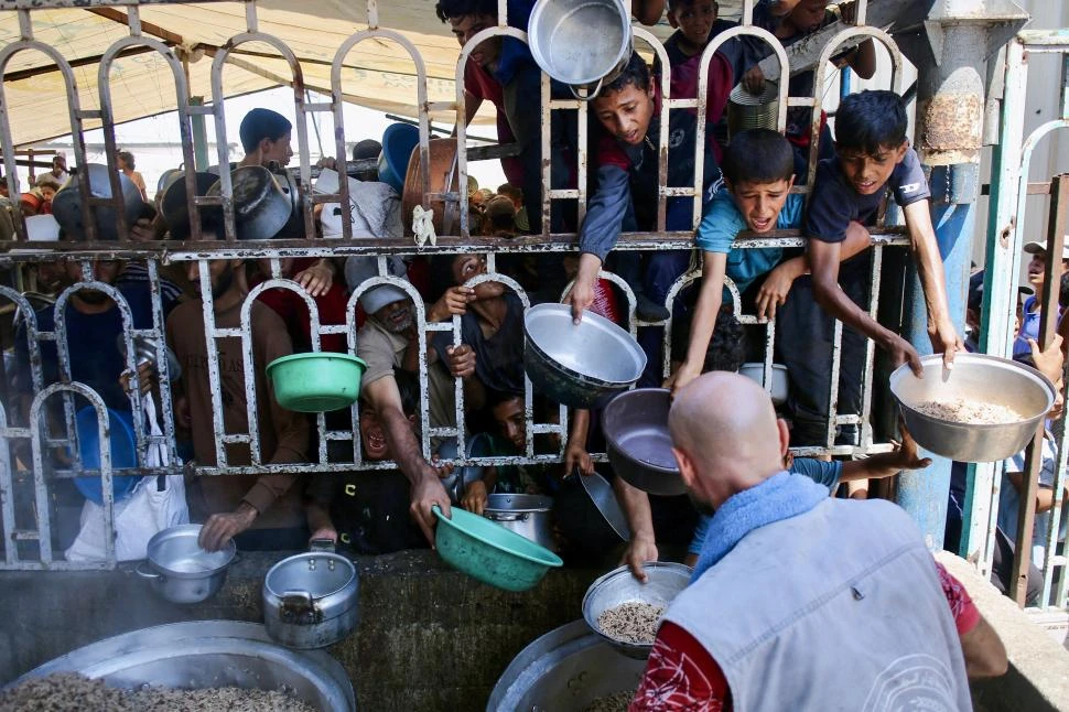 PANZAS VACÍAS. Los niños palestinos se agolpan para conseguir un plato de comida en la cocina comunitaria en el área de Mawasi, en Jan Yunis.  afp