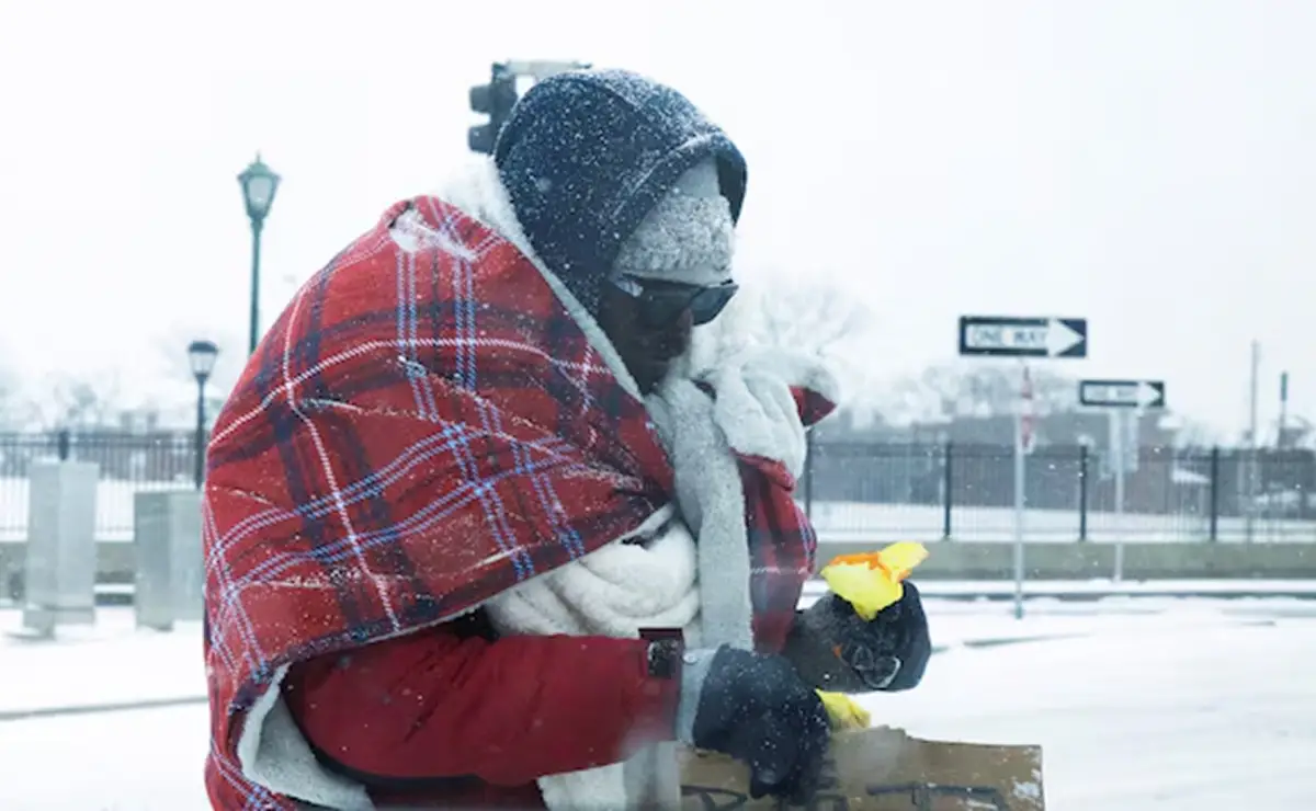 Un residente abrigado con varias mantas y gorros clasifica provisiones al aire libre en St. Louis 