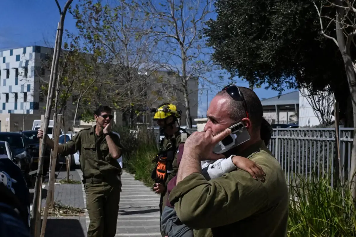 Un soldados israelí habla por teléfono mientras sostiene a su hijo durante la evacuación parcial de un edificio residencial.