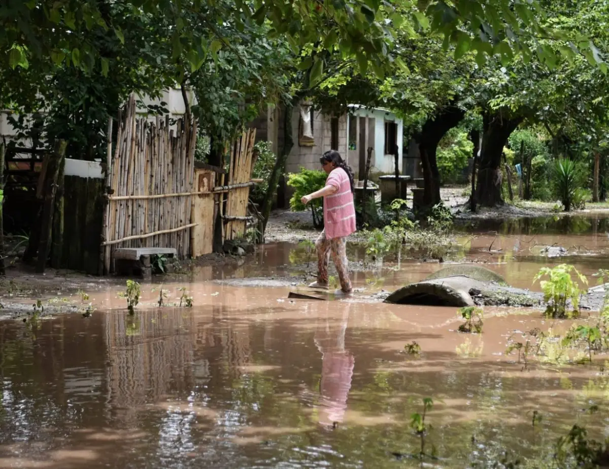 BARRO Y AGUA. Una vecina intenta cruzar por la vereda para llegar a su vivienda usando un puente improvisado de chapas y tablas de madera.